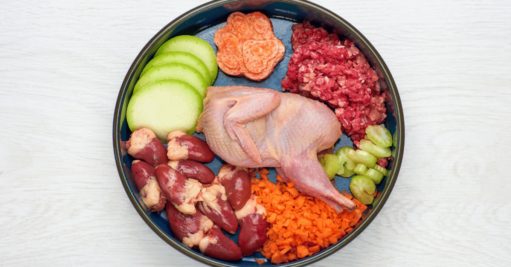 fresh chichen pieces in the middle of a dog bowl with other organ meat and vegetables 